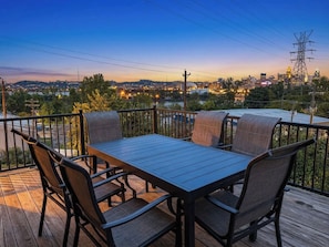 A deck with a table and chairs, overlooking a cityscape at dusk. - Near Cincy Skyline Views Historic 4BR (Covington)