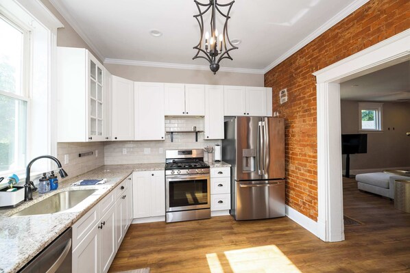 A modern kitchen with white cabinets, stainless steel appliances, and a brick accent wall. - Ludlow Lodge w/ City Views (Covington)