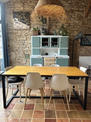 A dining area with a wooden table, white chairs, a stone wall, and a hanging light fixture.