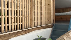 Une cloison en lattes de bois dans une pièce avec un escalier et une petite plante posée sur une étagère en bois.