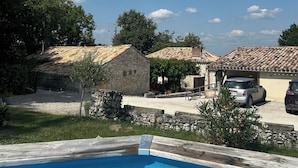Une piscine bordée de pierres, entourée d’une pelouse et de bâtiments en pierre aux toits de tuiles.