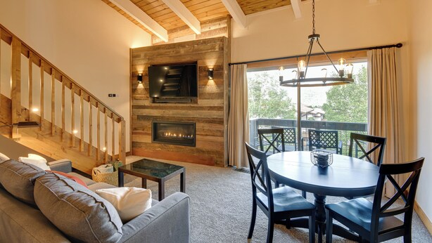 A cozy living room with a fireplace, a staircase, and a balcony with outdoor furniture. - Ski-in/ski-out Steamboat Condo w/ Slope-side Views (Steamboat Springs)