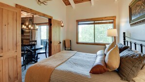 A bedroom with a large bed, a window, a wooden ceiling, and a dining area visible through an open door. - Ski-in/ski-out Steamboat Condo w/ Slope-side Views (Steamboat Springs)