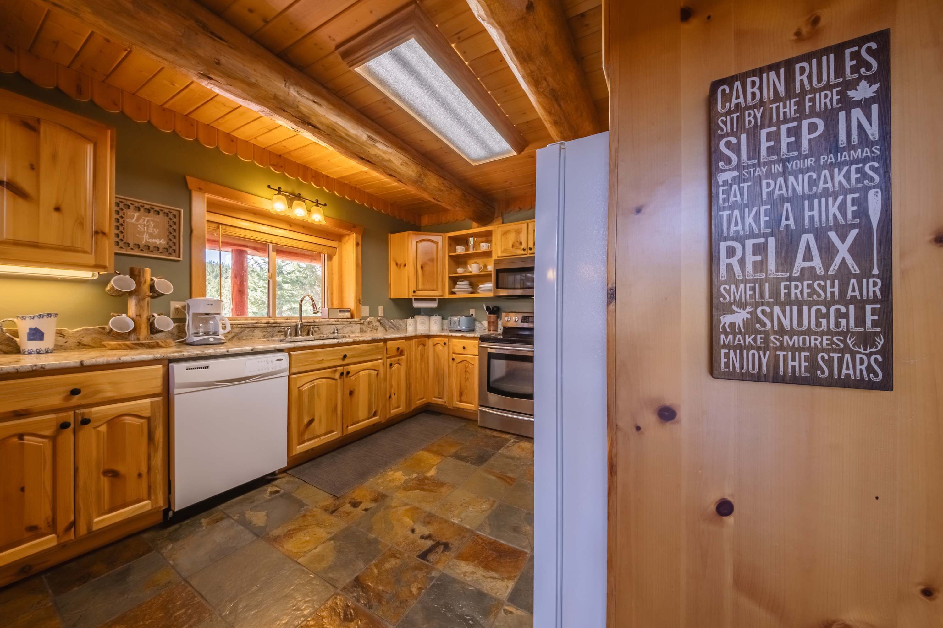 A cabin kitchen with wooden cabinets, a stone tile floor, and a sign listing cabin rules.