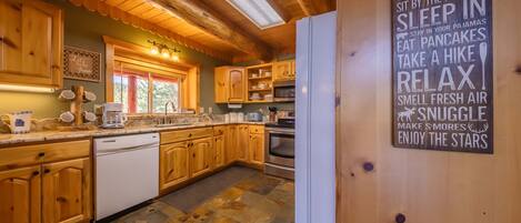 A cabin kitchen with wooden cabinets, a stone tile floor, and a sign listing cabin rules.