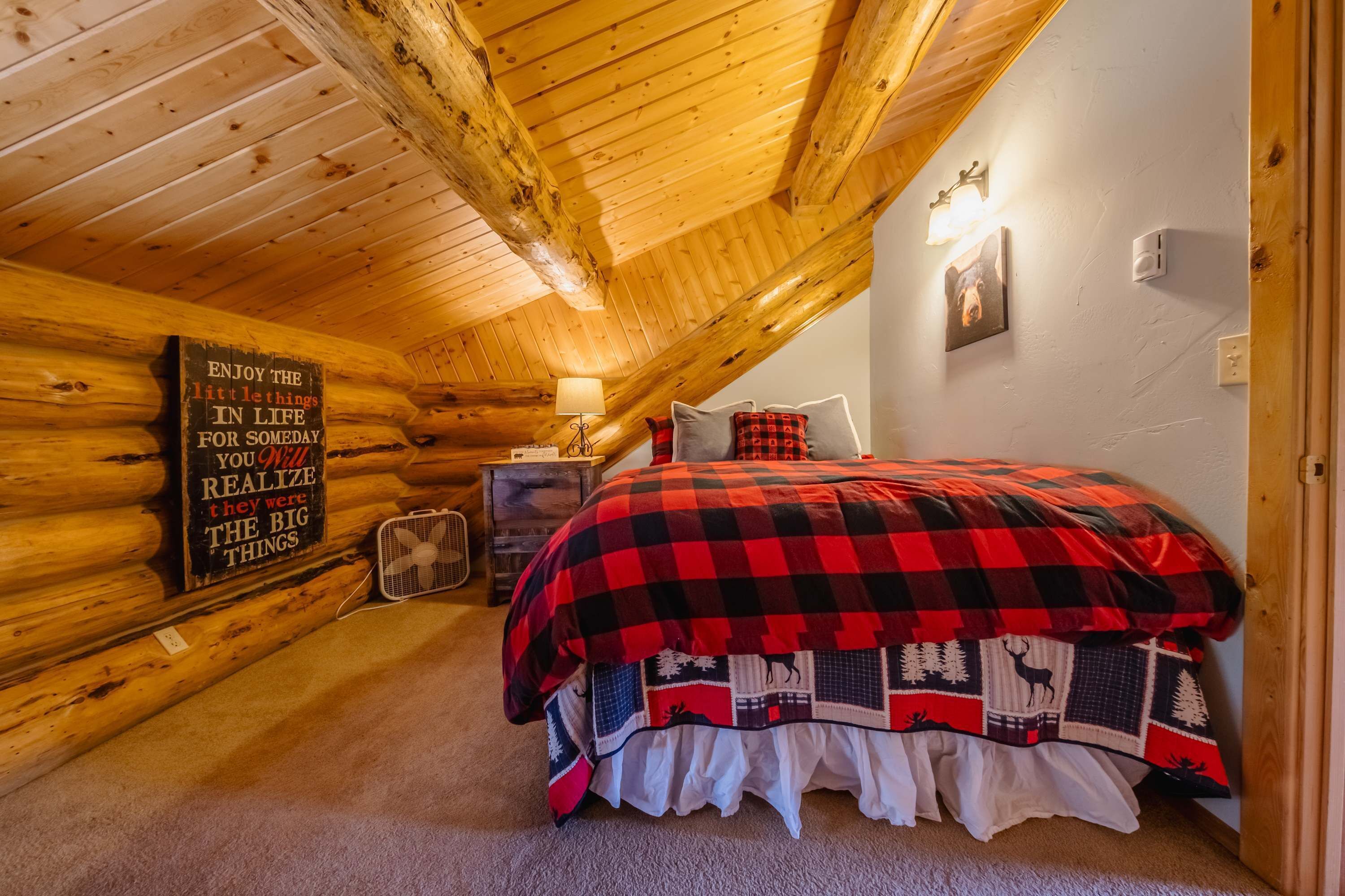 A cozy log cabin bedroom with a bed, a wall-mounted lamp, and a motivational sign.