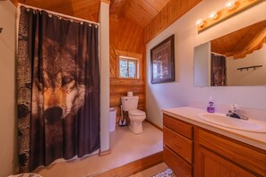 Features a large mirror above the sink, a wolf-print shower curtain, and a window above the toilet.