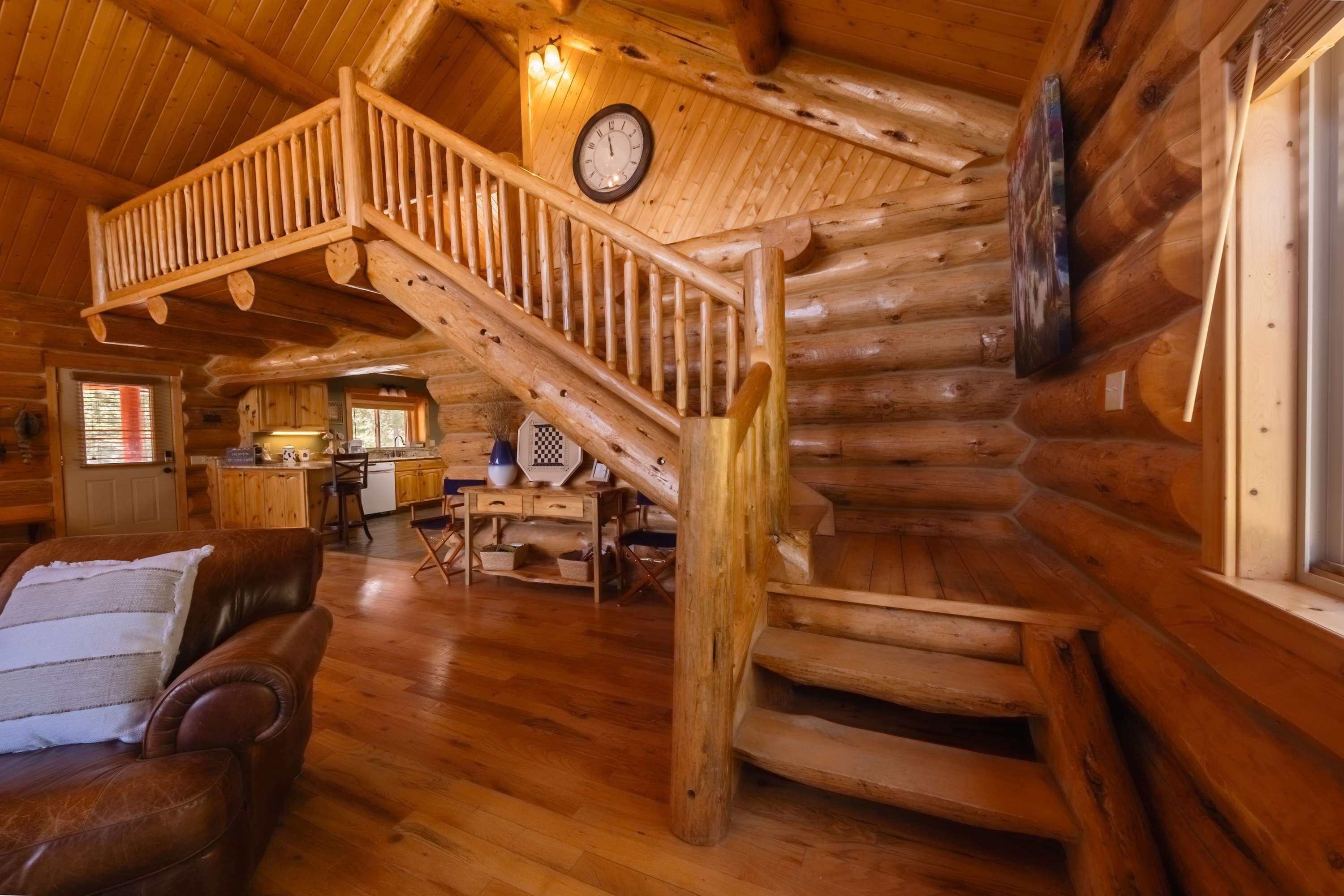 Interior de una cabaña de troncos con una escalera de madera, un comedor y una sala de estar con un sofá de cuero.