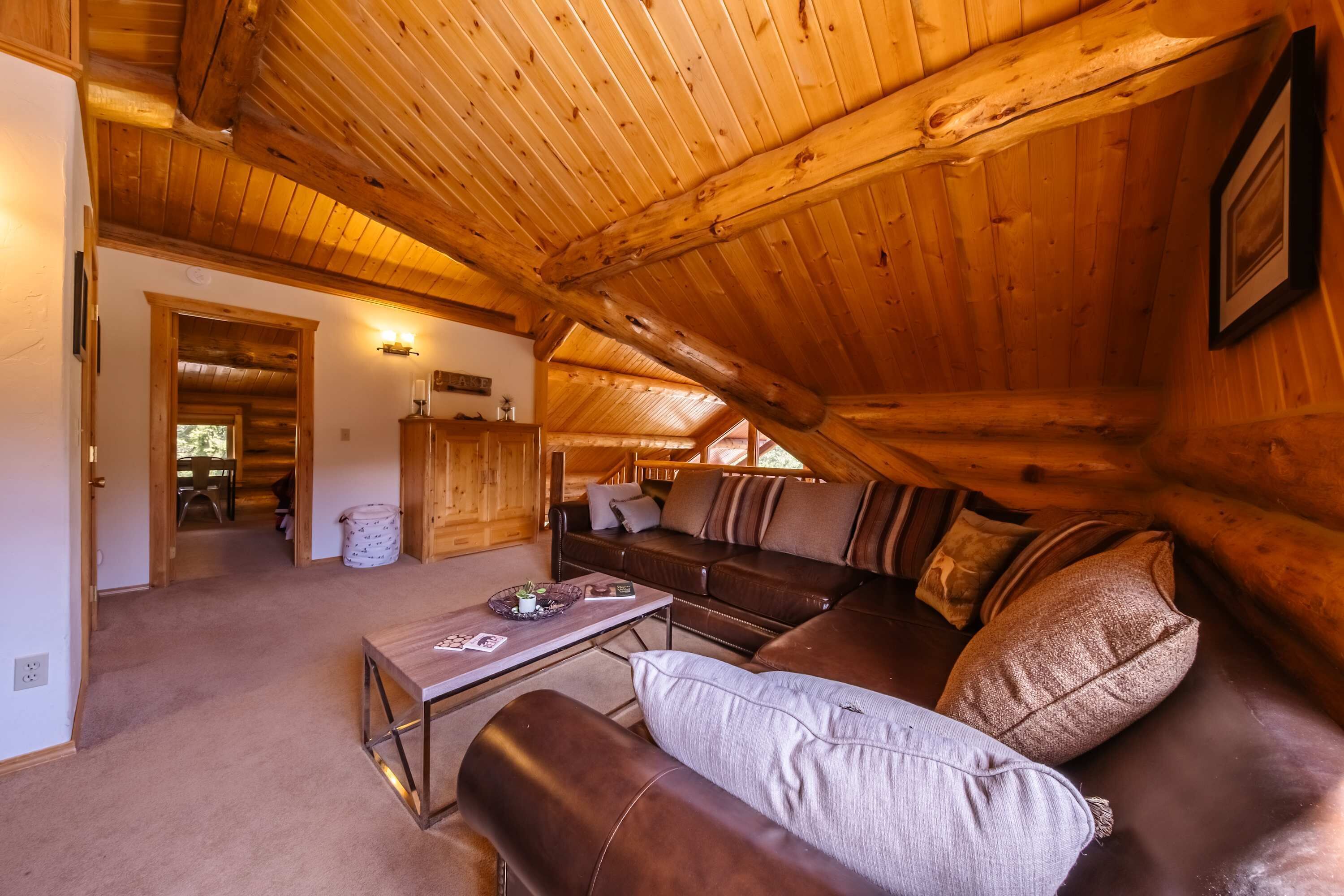 A cozy log cabin interior with a wooden ceiling, a sofa, a coffee table, and a fireplace.