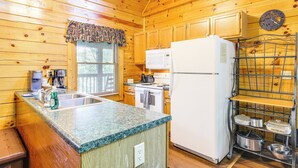Eine Holzhütte mit einer Küche, einer Granitarbeitsplatte, einem weißen Kühlschrank und einem Metallregal mit Töpfen und Pfannen.