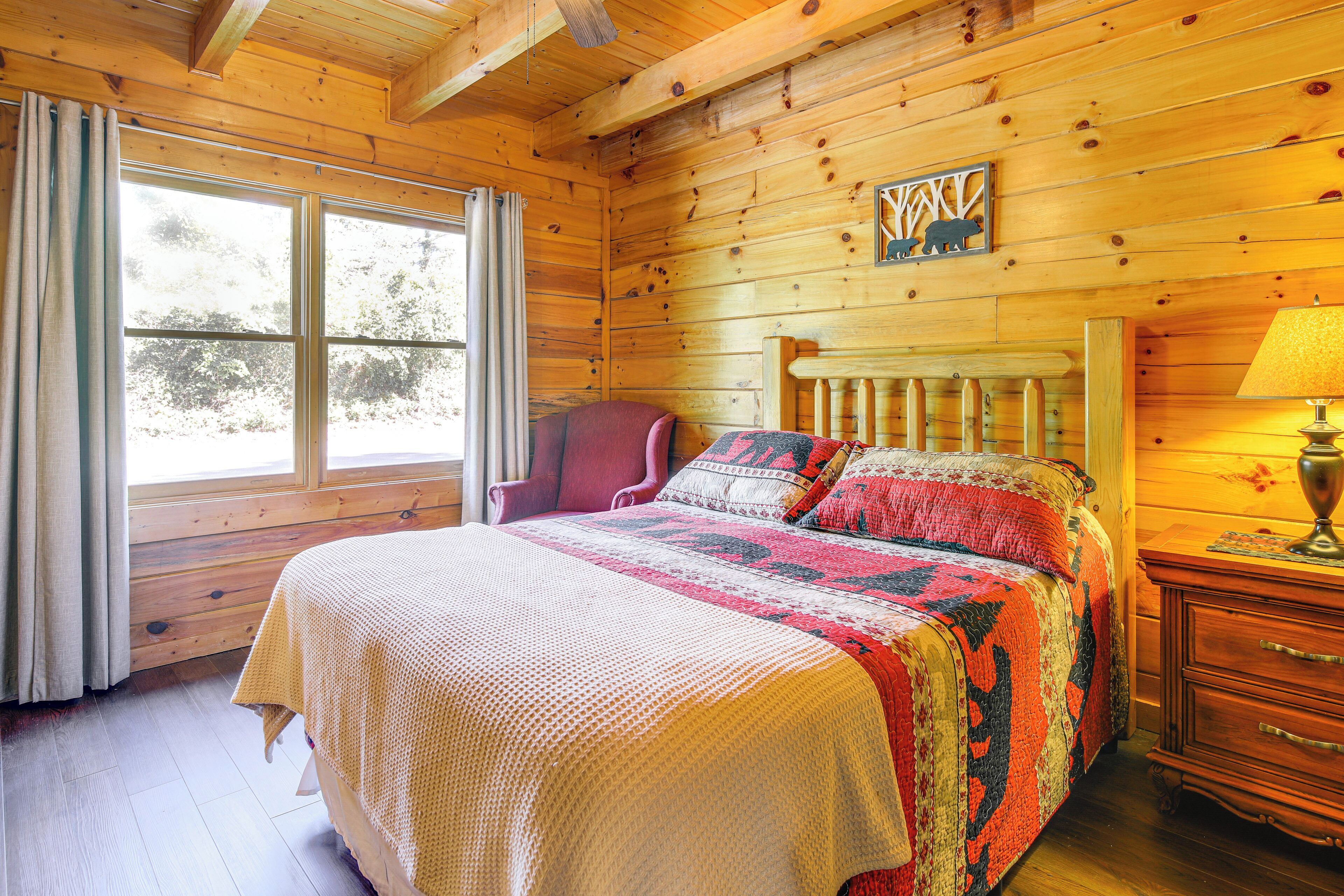 Dormitorio de una cabaña de madera con cama, una silla, una mesita de noche y una ventana.