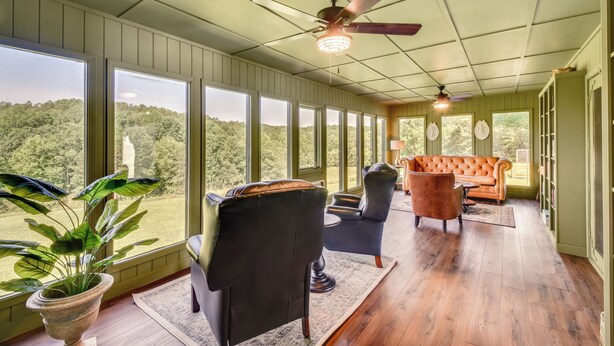 A spacious room with large windows, a ceiling fan, and a mix of seating including a sofa and chairs. - Home w/ Fire Pit on 27 Acres in Walhalla! (Walhalla)