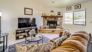 A living room with a stone fireplace, a television, and a brown leather couch. - Sedona Condo on Golf Course w/ Pool Access! (Sedona)