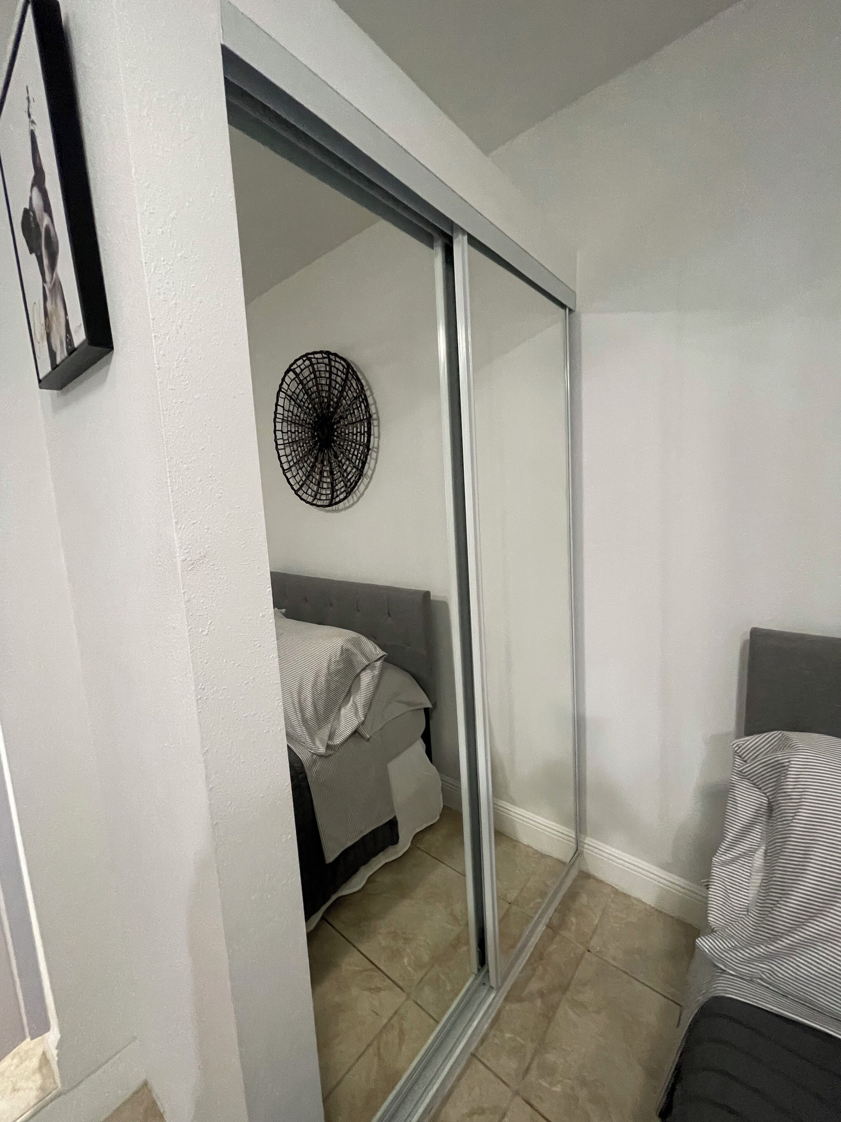 Een slaapkamer met een bed, een stoel, een spiegel en een decoratie aan de muur.