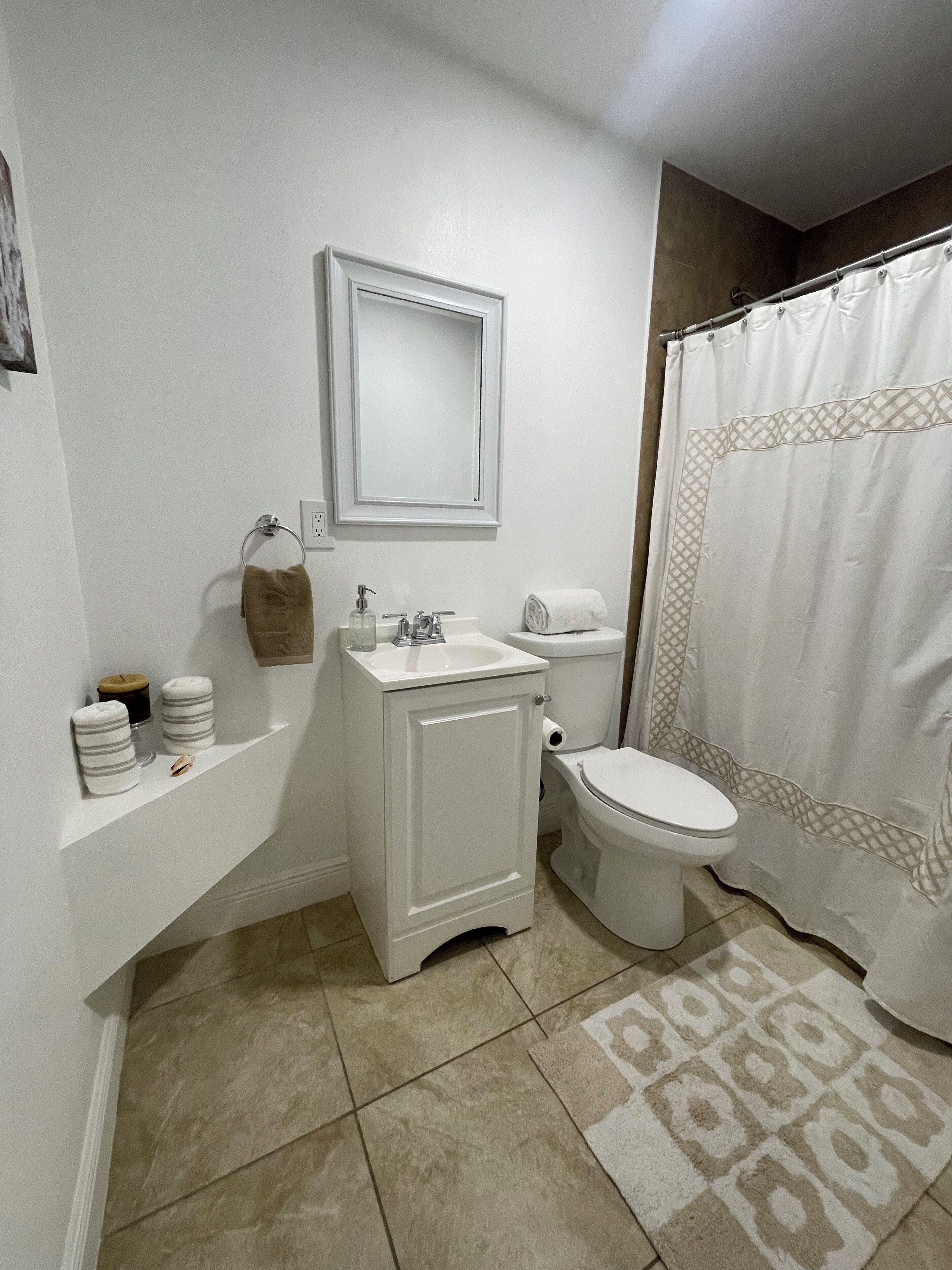 A small bathroom with a toilet, sink, and mirror. There are towels and a shower curtain.