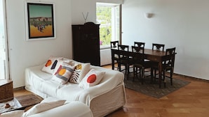 Ein Wohnzimmer mit Sofa, einem Esstisch mit Stühlen, einem Schrank und einem Bild an der Wand.