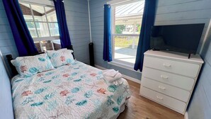 A bedroom with a bed, a dresser, a television, and a window with curtains.