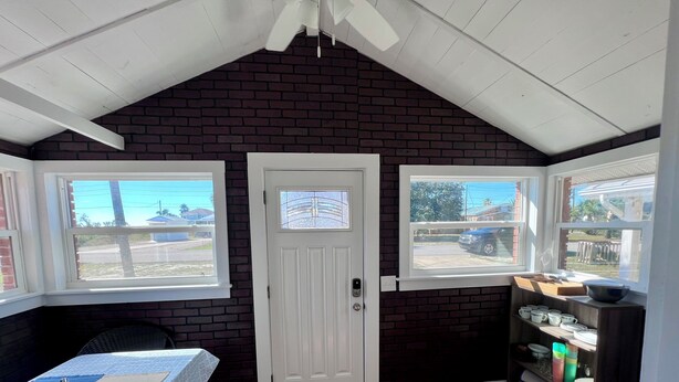 A room with a sloped ceiling, a white door, and two windows with views of the outside.