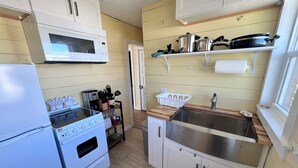 A compact kitchen with white cabinets, a microwave, a stove, a sink, and a window.