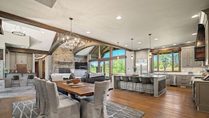 A spacious kitchen with a stone fireplace, wooden beams, and large windows offering views of the outdoors. - Golf Course Escape with Access to Exclusive Golf (Bend)