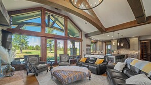A spacious living room with a large window, a fireplace, and a kitchen area. - Golf Course Escape with Access to Exclusive Golf (Bend)