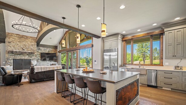 A spacious kitchen with a large island, bar stools, a stone fireplace, and a view of the outdoors. - Golf Course Escape with Access to Exclusive Golf (Bend)
