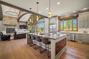 A spacious kitchen with a large island, bar stools, a stone fireplace, and a view of the outdoors. - Golf Course Escape with Access to Exclusive Golf (Bend)