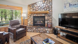 Una sala de estar acogedora con chimenea de piedra, sofá de cuero y televisor de pantalla plana.