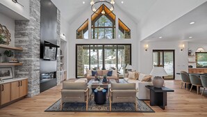 A spacious living area with a high ceiling, stone wall, and large windows offering a view of the outdoors. - Luxury Family Retreat with Access to Exclusive Golf (Sunriver)