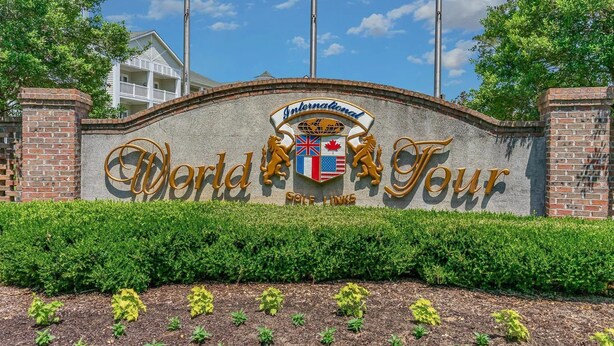 Señal del campo de golf World Tour con un muro de ladrillo, setos y un cielo azul claro.