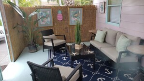 Un espace extérieur accueillant, aménagé avec des meubles en osier, un tapis bleu orné de motifs d’ancres et des plantes tropicales.