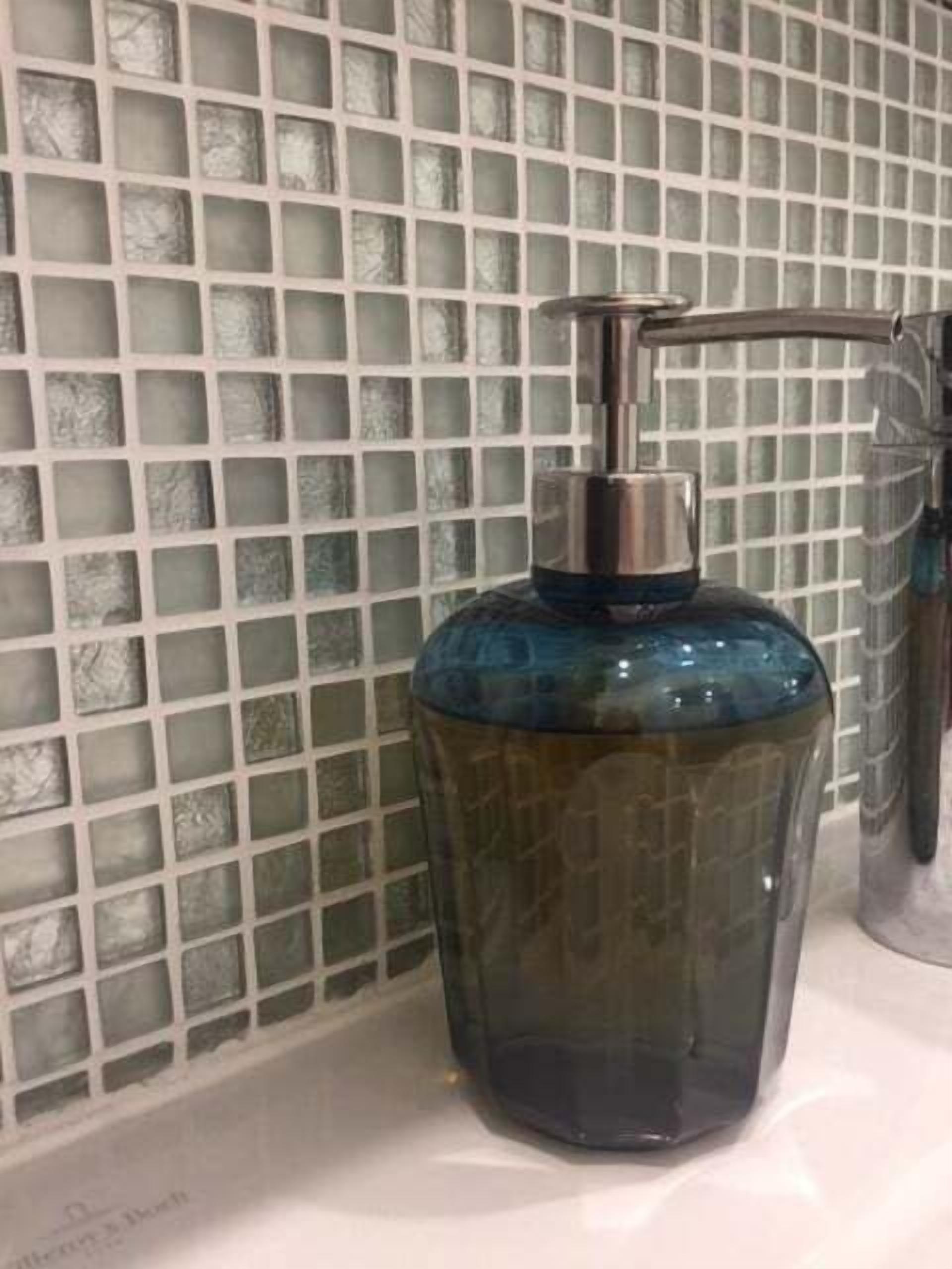 A bathroom with a glass mosaic wall and a blue soap dispenser on the sink.