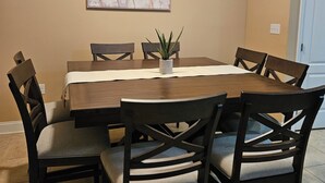 A dining area with a wooden table, six chairs, and a painting on the wall. - 10 mins to Navarre Pier! Everything YOU need! (Navarre)