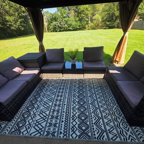 An outdoor seating area with a patterned rug, cushioned sofas, and a small table with a plant.
