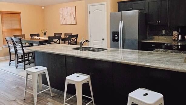 A modern kitchen with a central island, white bar stools, and a dining area with chairs and a table. - 10 mins to Navarre Pier! Everything YOU need! (Navarre)