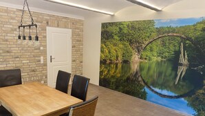 Ein Essbereich mit einem Holztisch und Stühlen, einer Ziegelwand, einer weißen Tür und einem Wandgemälde einer Flusslandschaft.