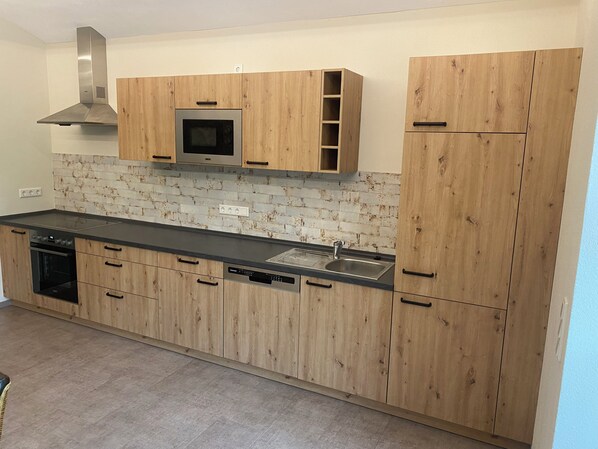 A modern kitchen with wooden cabinets, a stainless steel range hood, a built-in microwave, and a dishwasher.