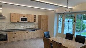 Eine moderne Küche mit Holzausstattung, einer eingebauten Mikrowelle und einem Essbereich mit Korbstühlen.