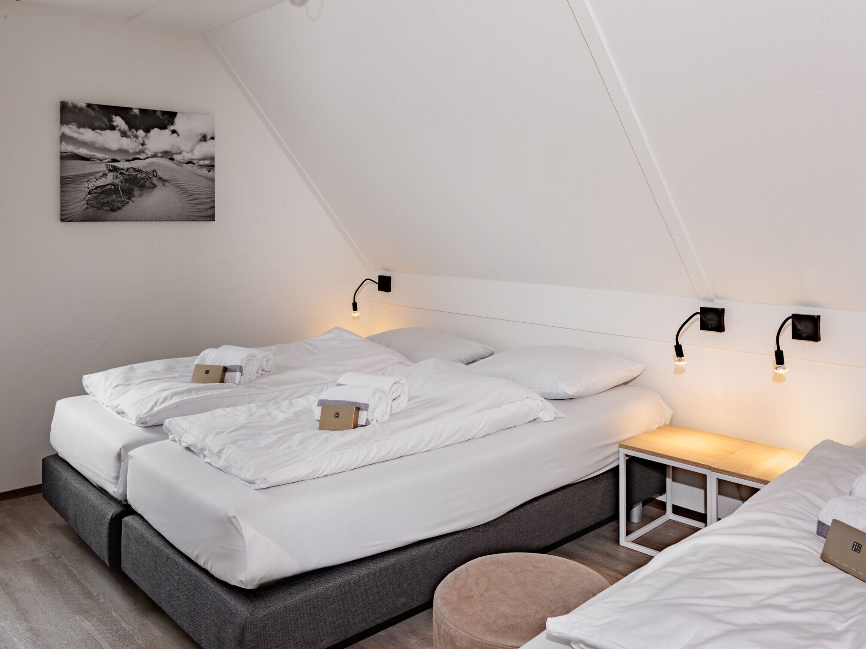 A modern bedroom with two beds, a bedside table, and a wall-mounted light fixture.