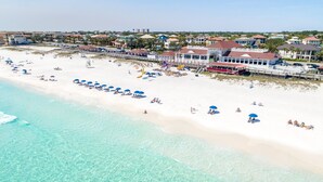 Egy tiszta, türkizkék vízű, fehér homokos strand, ahol több napernyő is található.