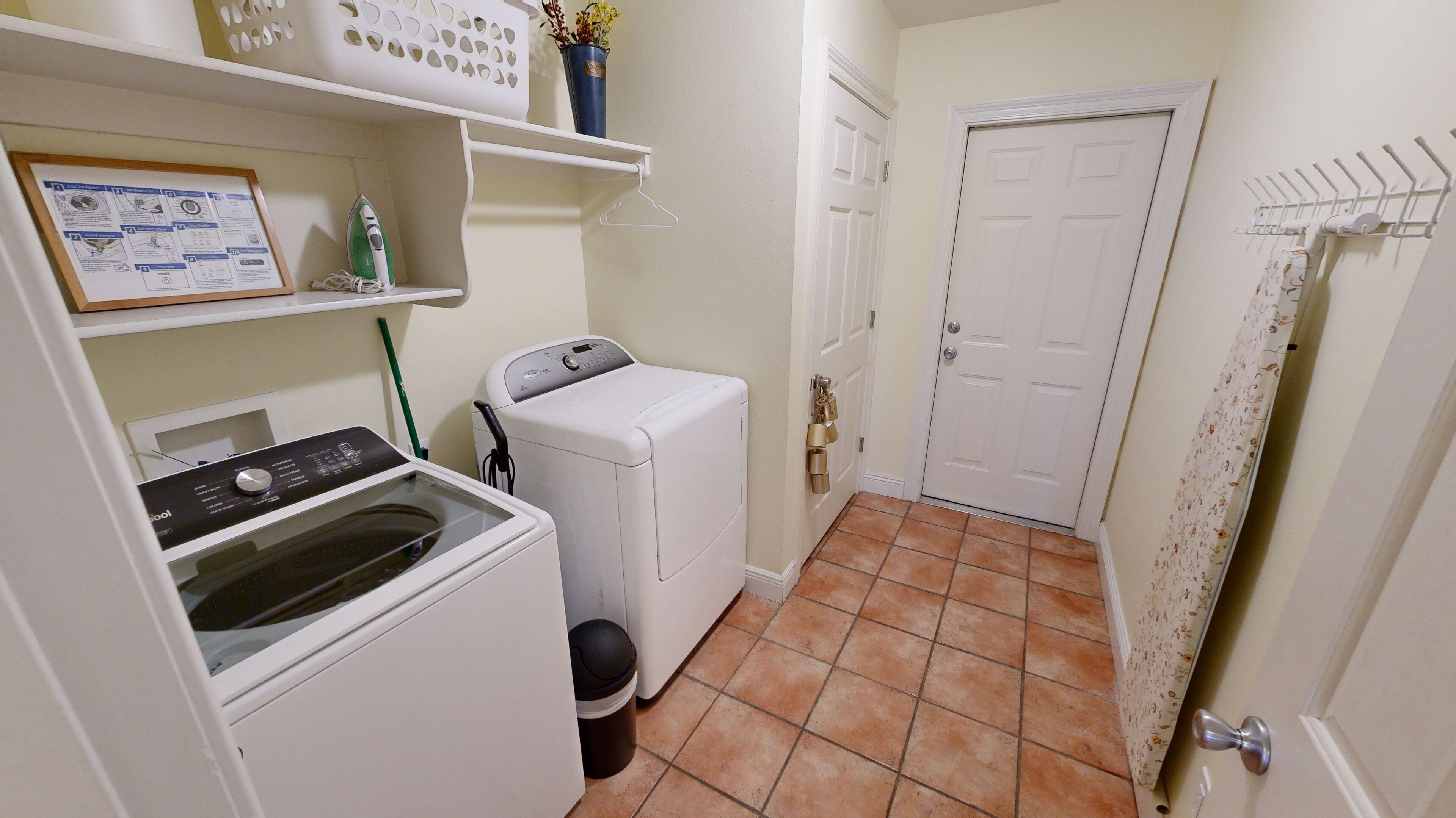 Une buanderie équipée d’un lave-linge, d’un sèche-linge et d’une planche à repasser fixée au mur.