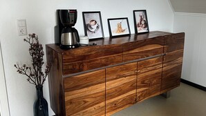 Een houten dressoir met een koffiezetapparaat en ingekaderde foto's erboven.
