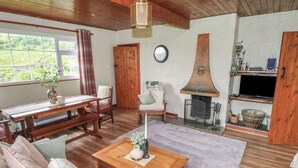 A cozy living room with a wooden bench, sofa, and coffee table. A fireplace with a decorative hood is visible, along with a television and a shelf with various items. - BEN GOWER, pet friendly, with open fire in Oughterard, County Galway (GAILLIMH)