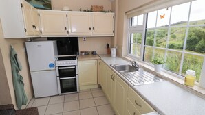 A compact kitchen with a stove, oven, sink, and a window with a view of greenery. - BEN GOWER, pet friendly, with open fire in Oughterard, County Galway (GAILLIMH)