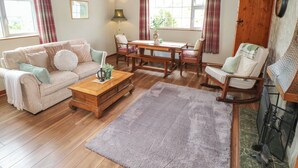 A cozy living room with a wooden ceiling, a sofa, a coffee table, a rocking chair, and a fireplace. - BEN GOWER, pet friendly, with open fire in Oughterard, County Galway (GAILLIMH)