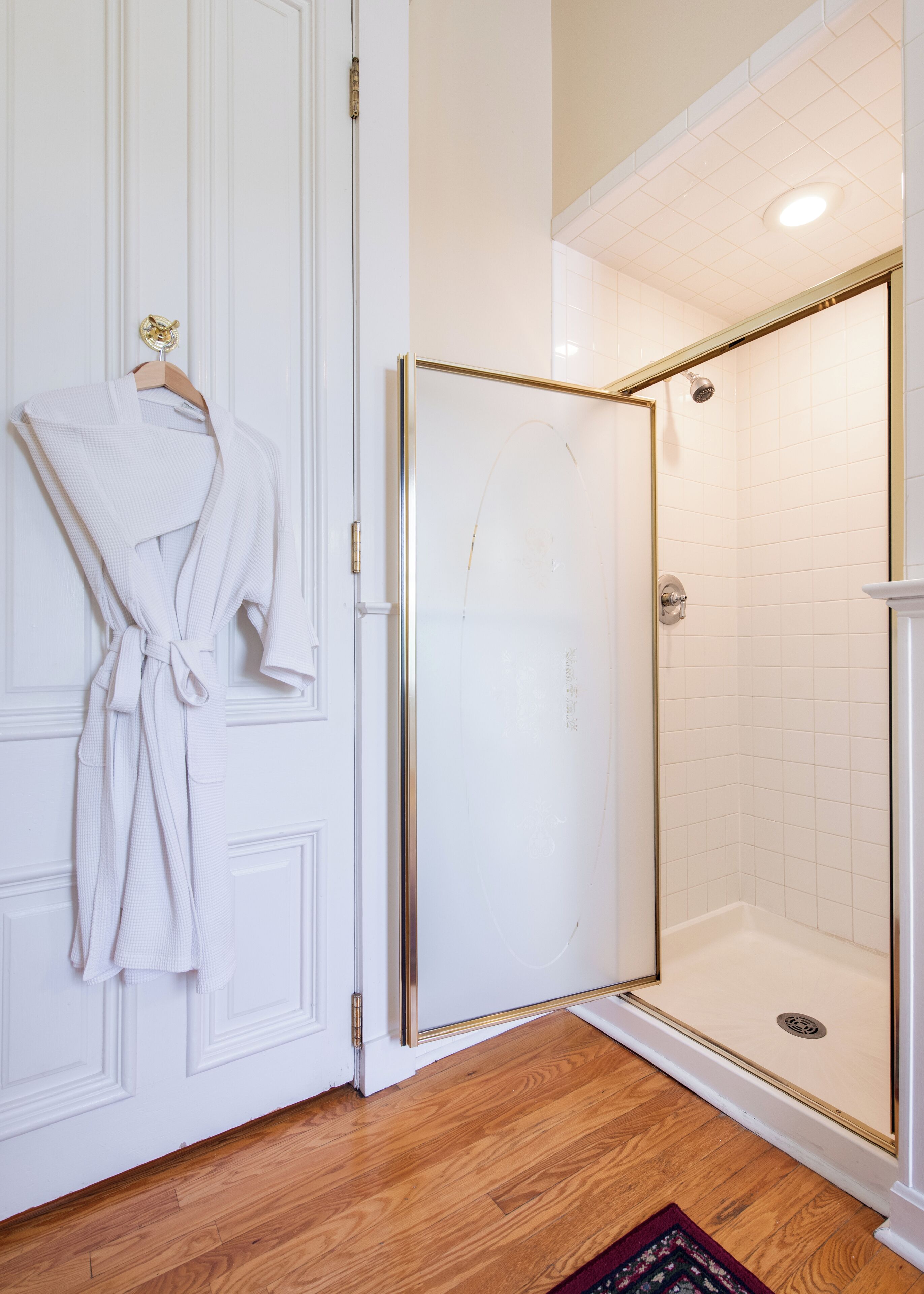 A bathroom with a white door, a glass shower enclosure, and a wooden floor.