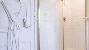 A bathroom with a white door, a glass shower enclosure, and a wooden floor.