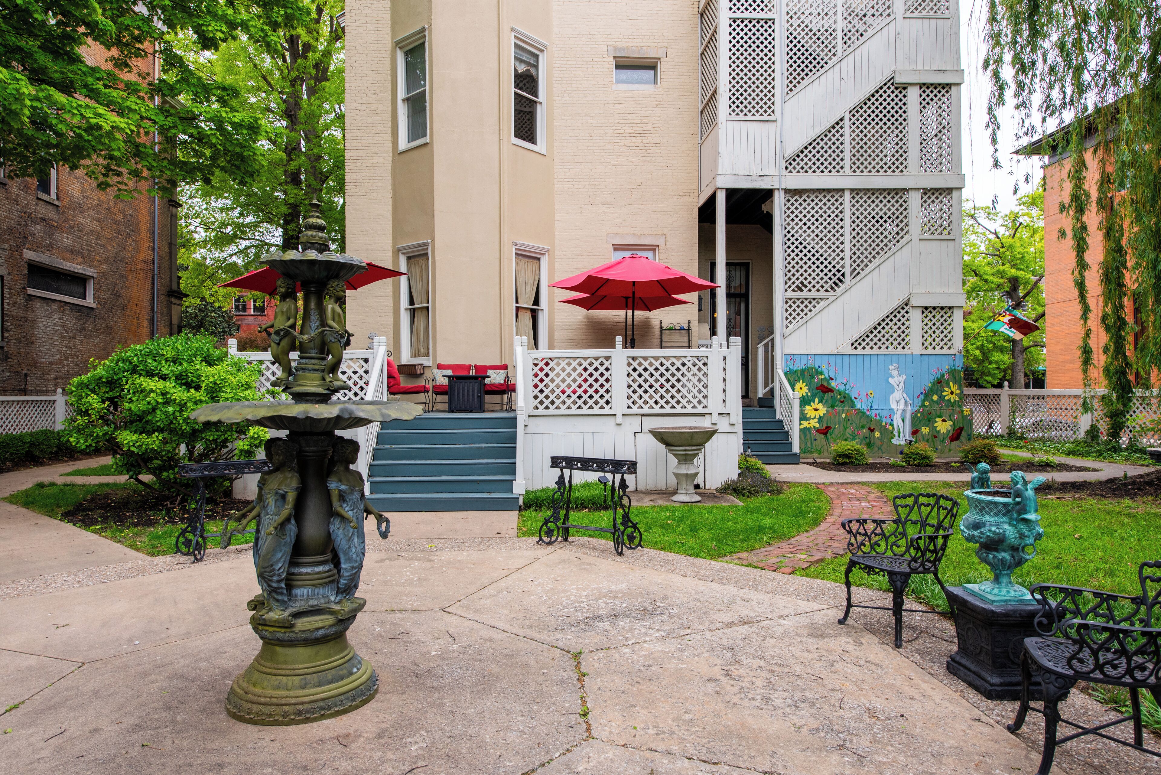 A courtyard with a fountain, outdoor seating, and a building with a white fence and steps.