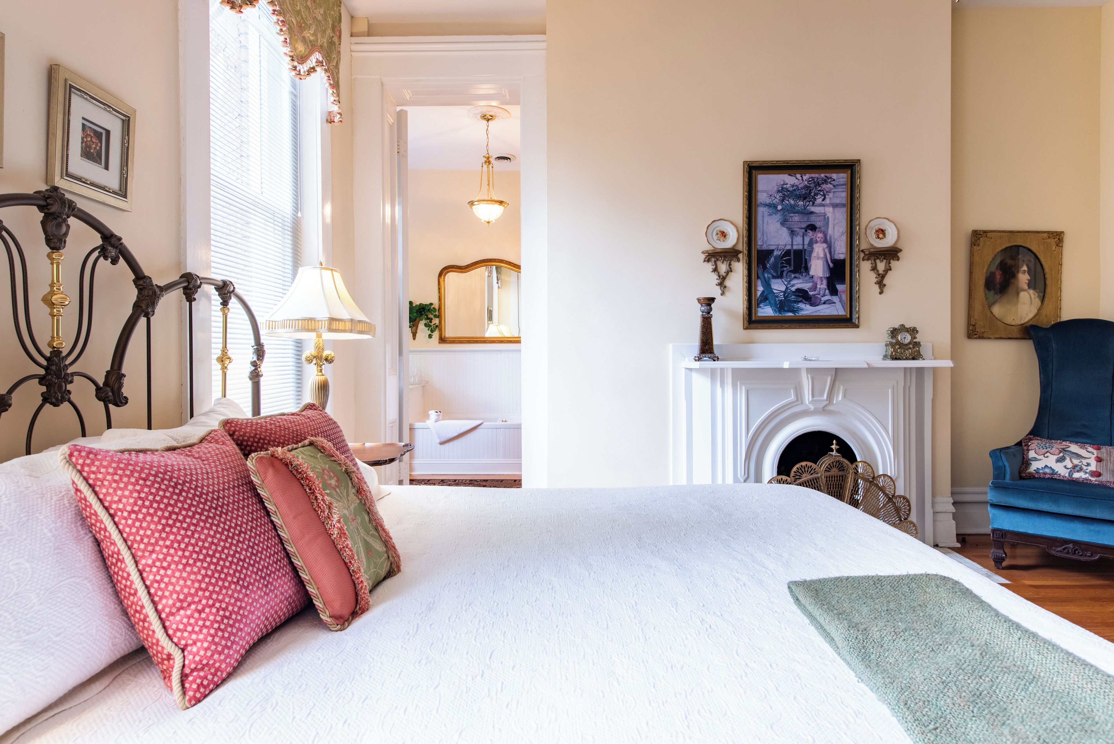 A bedroom with a large bed, a fireplace, and a blue armchair.