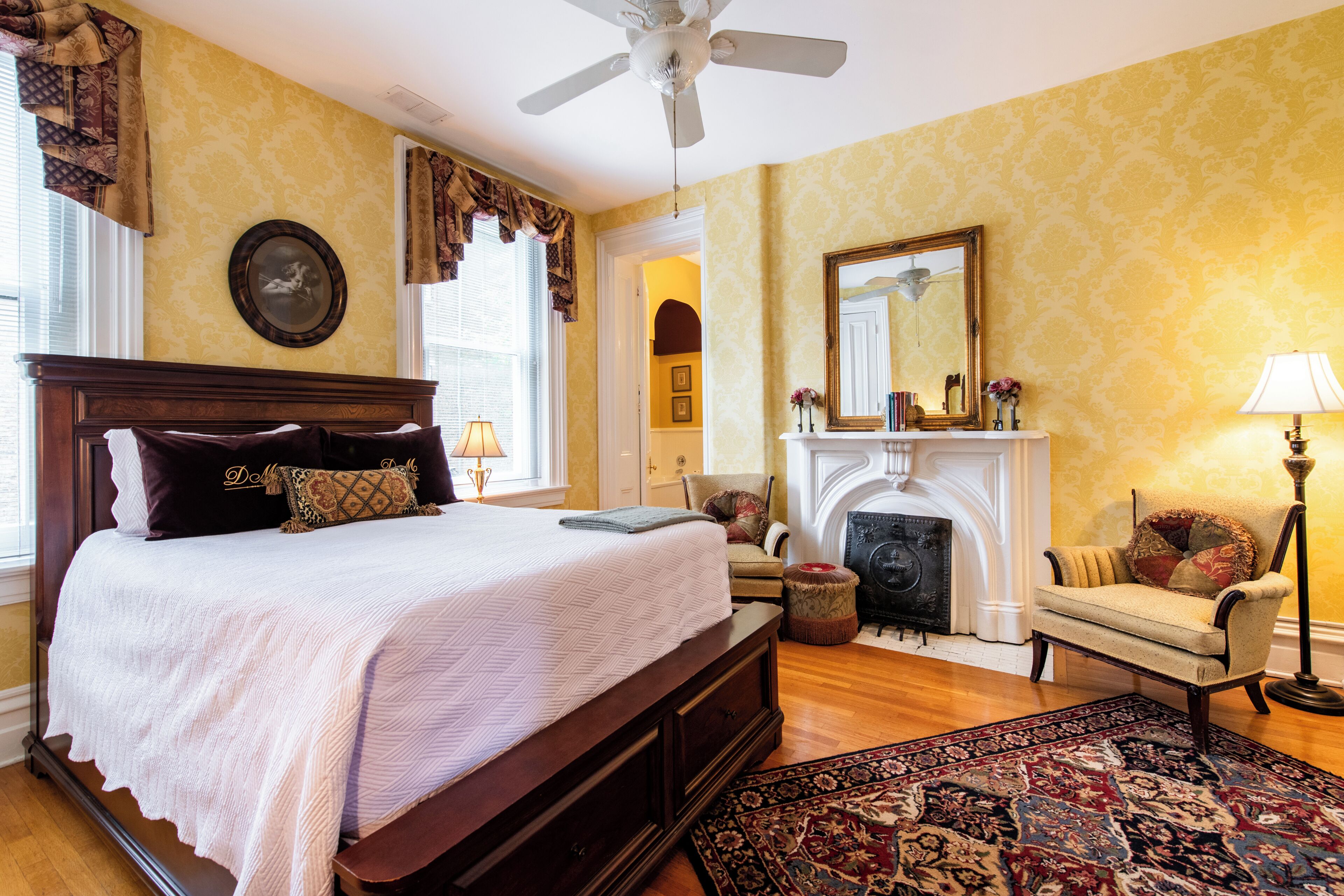 A bedroom with a large bed, a fireplace, a chair, and a ceiling fan.